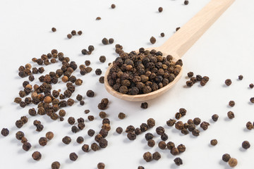 blask pepper peppercorns in wooden spoon isolated on white background. Closeup. © eyecon