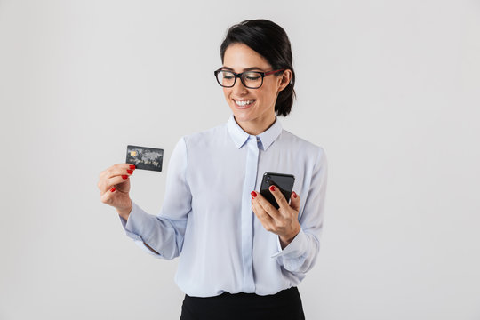 Image of confident office woman wearing eyeglasses holding mobile phone and credit card, isolated over white background