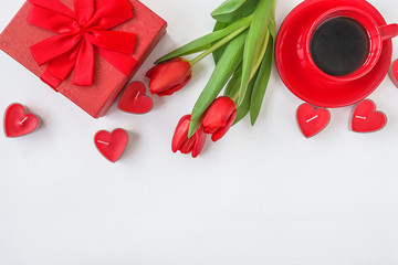 Beautiful valentine's day background: red gift box, bouquet of red tulips, red cup of coffee and red candles on white background