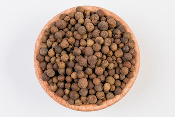 Allspices or Jamaica pepper in wooden bowl isolated on white background. Top view.