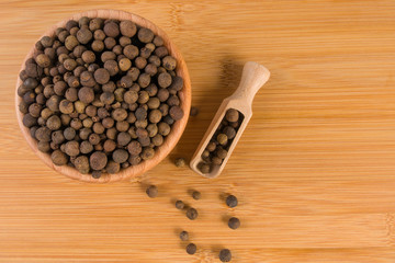 Allspices or Jamaica pepper in wooden scoop and bowl on bamboo desk. Top view.