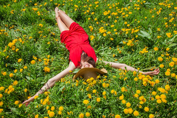 Young woman in red dress is laying on the grass full of yellow flowers.