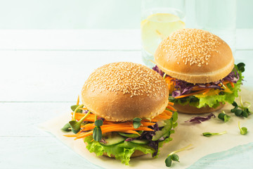 Appetizing burger from fresh sesame buns and raw vegetables and young sprouts blue light background.Healthy nutrition
