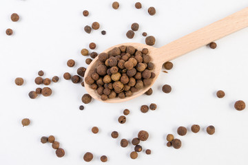 Allspices or Jamaica pepper in wooden spoon isolated on white background. Closeup.