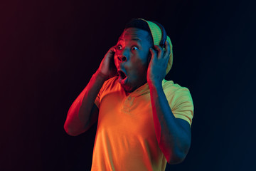 Young handsome happy hipster man listening music with headphones at black studio with neon lights. Disco, night club, hip hop style, positive emotions, face expression, dancing concept