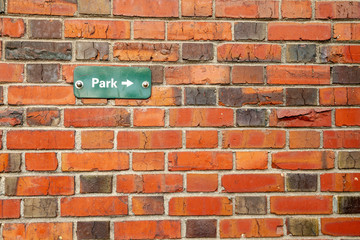 Fototapeta na wymiar Background image of a rustic red brick wall with a sign pointing to a park