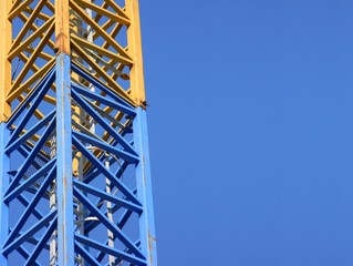 Fototapeta na wymiar Yellow and blue construction crane mast against blue sky