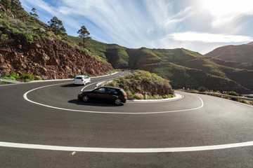 Asphalt road up, on which go two cars with tourists.