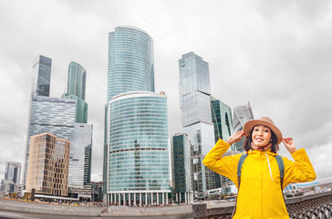 Fototapeta na wymiar Happy woman traveler in yellow coat against the background of a skyscrapers business center of a Moscow city. Vacation and business in Russia concept