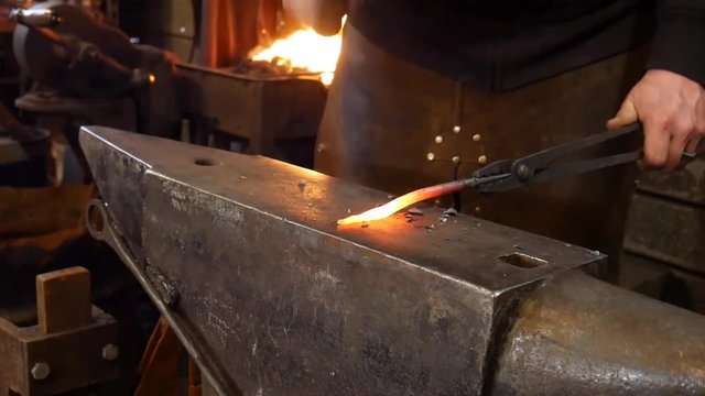 A Blacksmith Tapering a Molten Metal Bar of Steel at the Anvil by Hammering in the Blacksmith Shop