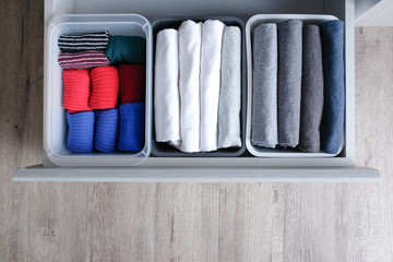 Close up stack of folded t shirt black gray white color and folded bright colorful socks in plastic baskets in a closet drawer in natural light. Room cleaning and tidying up concept. Top view.