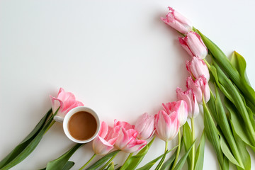 Pink tulips flat lay in a half circle with a cup of coffee on a white background