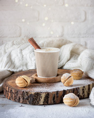 Cappuccino with cinnamon in a cup, beside a cookie, behind is a white background and beautiful bokeh from the yellow lights of a garland