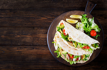 Pita bread sandwiches with grilled chicken meat, avocado, tomato, cucumber and lettuce served on  wooden background. Close up. Top view. Healthy fast food concept.