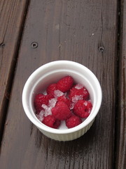 Red Raspberries in Pink or White Mug or Ramekin in Snow in Winter on Dark Wood Background