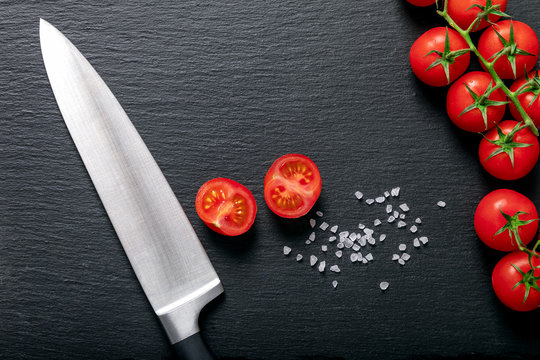 Frische, rote Tomaten mit Messer und Salzkörnern auf schwarzem Schiefrstein mit Textfreiraum