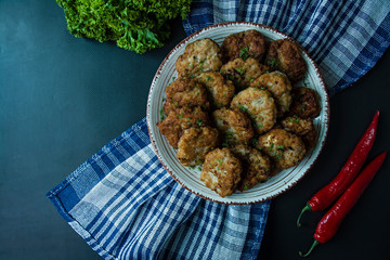 Pork cutlets on a plate with greens and vegetables on a black background. View from above