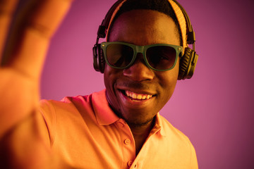 The young handsome happy hipster man listening music with headphones at black studio with neon...