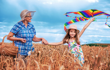 Childhood in the wheat field. Little girl and her grandmother have fun with kite. Childhood,...