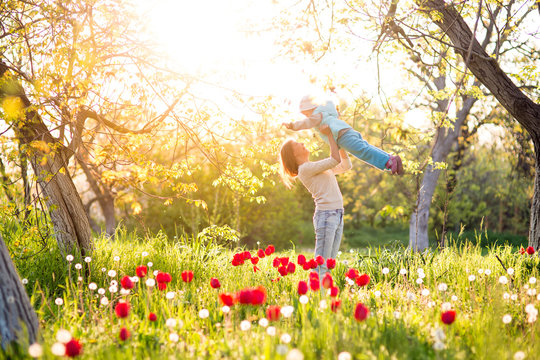 Family mom with daughter woman with child in spring stand and hug on a glade with green grass and tulips