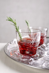 Two holiday red cocktails with rosemary on a metal tray with ice, grey background