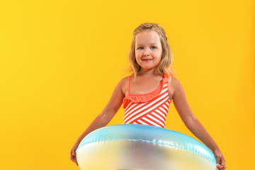 Adorable little child girl in a bathing suit with a swimming ring on a colored yellow background. Vacation concept