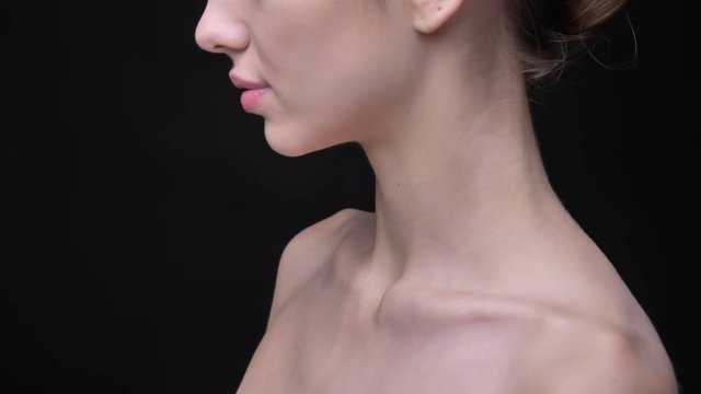 Close-up portrait in profile of female collarbone on black background.
