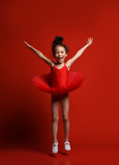 Cute little girl ballerina dancer in beautiful dress is dancing jumping on red background 