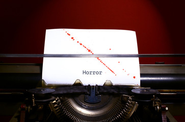 Typewriter spelling horror on paper with blood splashes