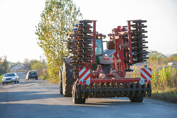 Tractor combine with disc harrows driving along rural road on sunny day. Agricultural machinery and farming concept. © bilanol