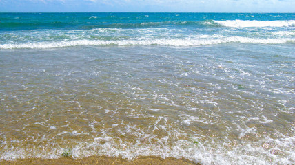 Sea salty pure blue waves roll on the sand of the local beach. Low waves on a sunny day.