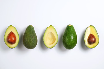 Minimal composition with whole and halved nutrient dense avocado fruit slices full of heart healthy monounsaturated fat on gray glass table top. Close up, copy space, top view, background.