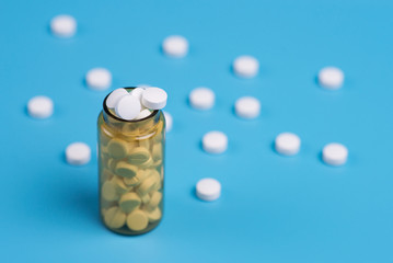 White pills in the glass bottle on a blue background.