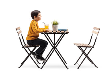 Little boy sitting alone at a table with orange juice