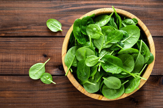 Fresh spinach leaves on wooden background. Healthy vegan food. Top view.