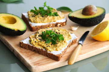 Vegan sandwich, rye bread guacamole toast with lactose free cheese spread. Nutrient dense avocado based superfood full of heart-healthy monounsaturated fat. Close up, copy space top view, background.