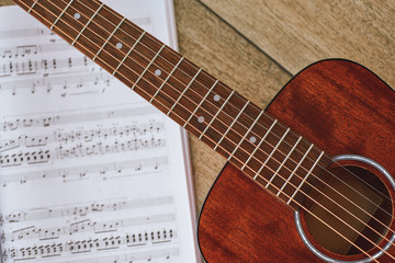 Plakat Playing Guitar. Close up view of brown acoustic guitar with music notes against wooden floor