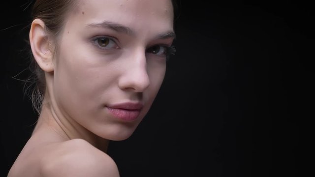 Portrait of young and slim caucasian girl with nude make-up moving slowly and watching softly in camera on black background.