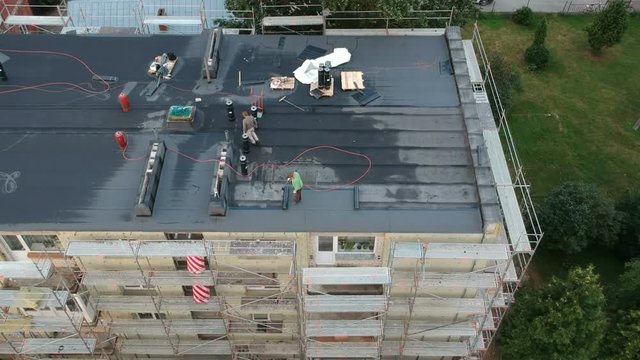 Workers roofers repair flat house roof in city, aerial view