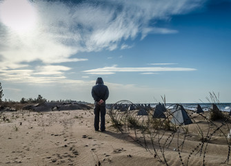 man walking near anti-tank barriers and barbed wire on the seashore