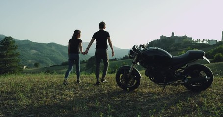 Young romantic couple spending a good time at nature in the middle of amazing landscape they arrived with their black motorcycle - Powered by Adobe