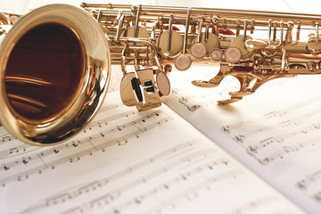 Closeup of a beautiful and shiny golden saxophone lying on music notes.