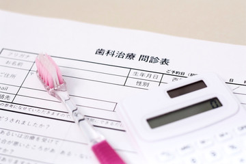歯の治療の問診票とピンクの歯ブラシと電卓、歯医者の予約と費用計算