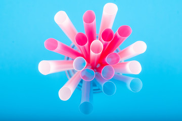 Colorful big plastic straws top view on a blue background used as an accent . Earth movement, plastic recycling and refuge theme. Blue,pink,white color.