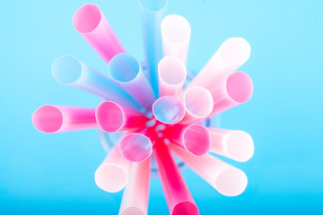 Colorful big plastic straws top view on a blue background used as an accent . Earth movement, plastic recycling and refuge theme. Blue,pink,white color.