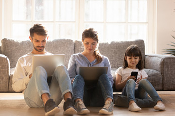 Family with kid sitting on floor at home using devices