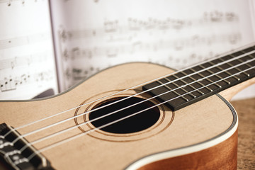Ukulele chords. Close-up photo of ukulele guitar and music notes against of wooden background....