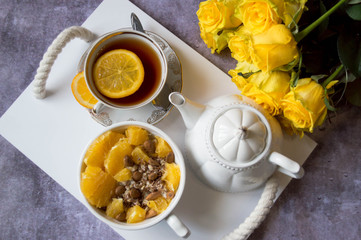 A pleasant surprise in bed for your beloved woman in the form of oatmeal breakfast with oranges and a cup of tea and a bouquet of yellow roses.