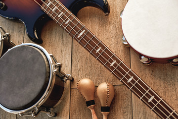 Naklejka premium Na próbie w studio. Widok z góry zestawu instrumentów muzycznych: brązowa gitara elektryczna, perkusja, złote marakasy i tamburyn leżący na drewnianym tle