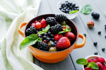 Berries in bowls on wooden background. Composition of raspberry, currant, strawberry, blueberries,...